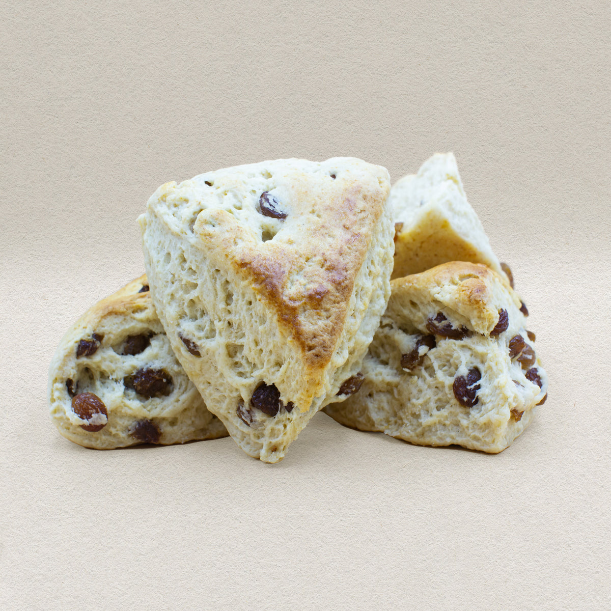 Four rustic looking triangular raisin scones with a golden crust and fluffy white center filled with juicy raisins.