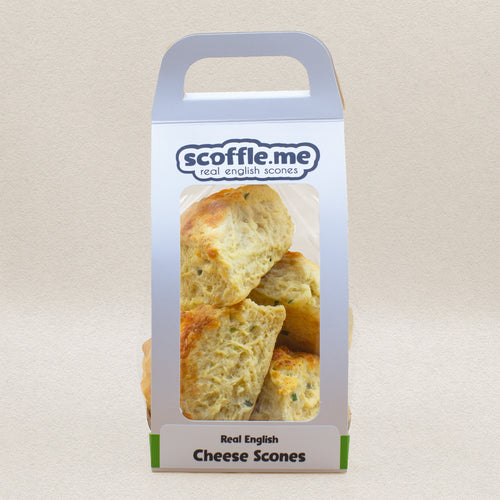 A cute white handled bag showcasing four delicious and rustic looking savory scones baked with cheddar cheese and chive.
