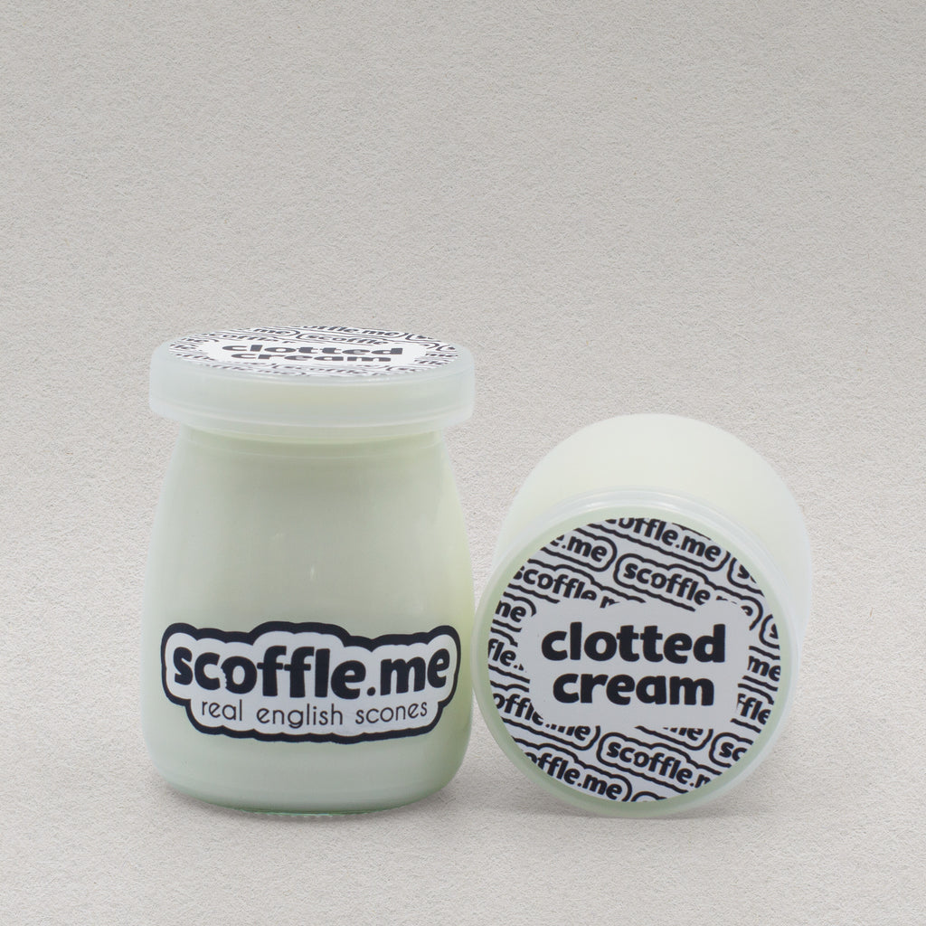 Two glass jars of Scoffle Me's homemade clotted cream placed so you can see the front and top view of the product packaging.