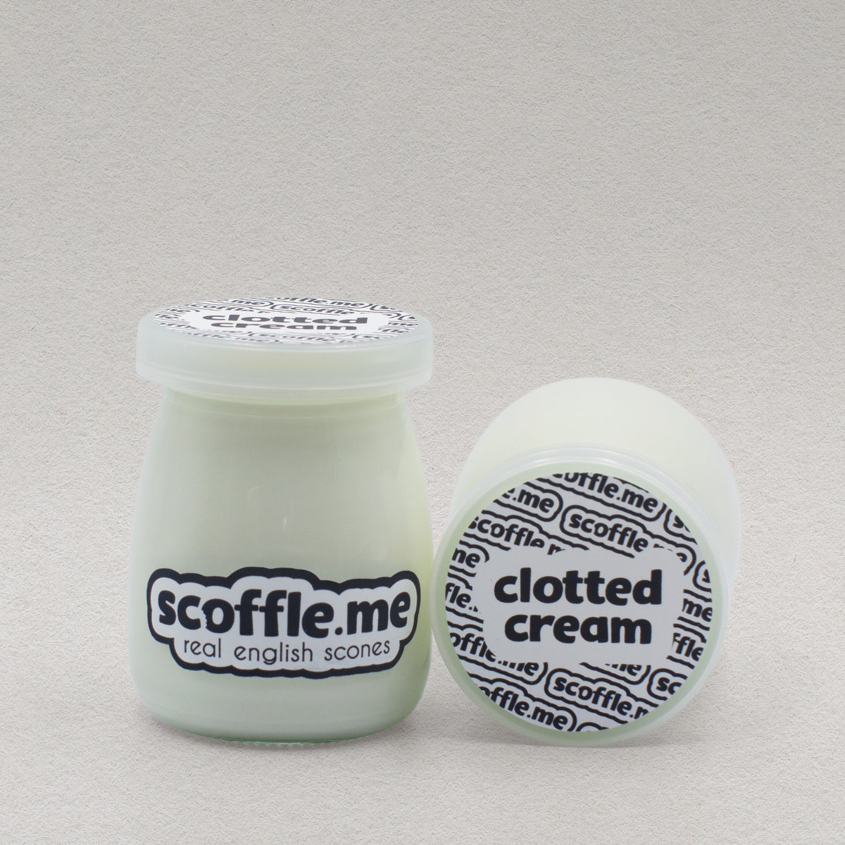 Two glass jars of Scoffle Me's homemade clotted cream placed so you can see the front and top view of the product packaging.